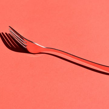 Shiny silver fork placed on a bright red background, casting a shadow.