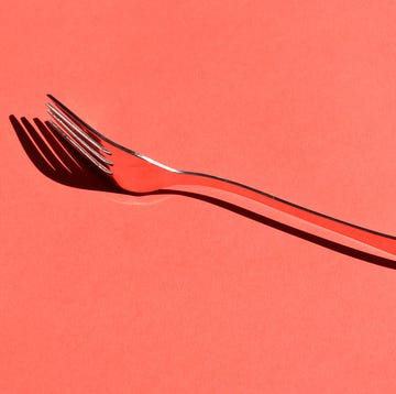 A close-up of a shiny metal fork casting a shadow on a vibrant red table, evoking a sense of simplicity and modern design Shiny silver fork placed on a bright red background, casting a shadow.