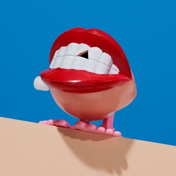 A playful, stylized mouth with red lips and white teeth positioned above a pastel surface against a bright blue background.