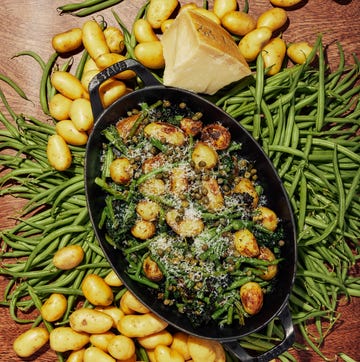 a dish with baby potatoes and green beans on a table scattered with more baby potatoes and green beans.