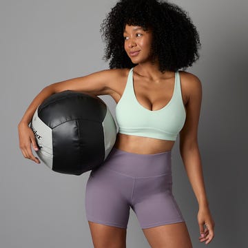 Young woman in athletic wear holding a medicine ball, smiling against a neutral background. Young woman in athletic wear holding a medicine ball, smiling against a neutral background.