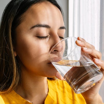 Young Latin American woman drinking a glass of fresh water standing close to the window in the morning. Healthy lifestyle and people concept. young latin american woman drinking a glass of fresh water standing close to the window in the morning. healthy lifestyle and people concept.