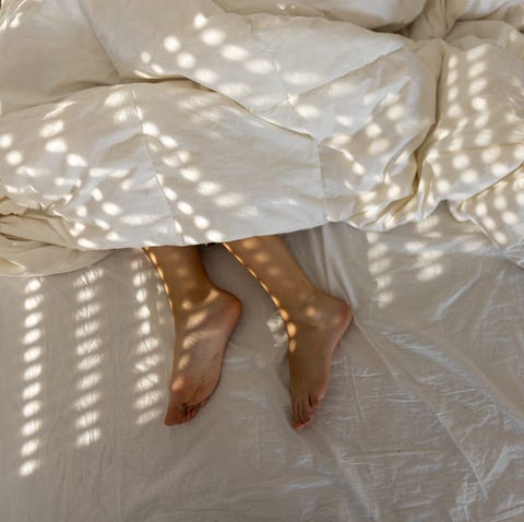Woman's legs while sleeping in bed covered with blanket young woman sleeping in her bed, in the photo are her feet, not covered with duvet