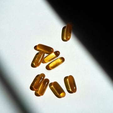 many oval shaped translucent golden fish oil capsules on a white table surface under the sunlight close up of pills with hard shadows and blank space for designs wellness, healthcare, healthy nutrition concept
