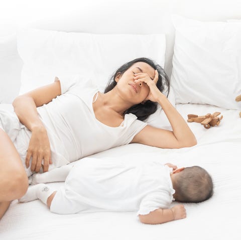 tired exhausted mother sleeping sleep with baby on white bed. overwhelmed new asian mom feeling sleep deprived and fatigued with infant at bedroom.