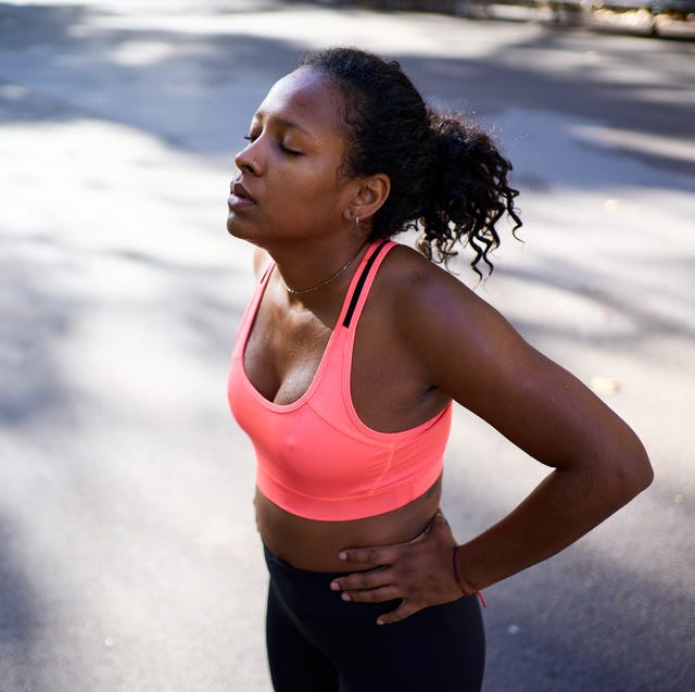 young african american woman taking a break during her outdoor exercise routine, breathing deeply with hands on hips and eyes closed. copy space image.