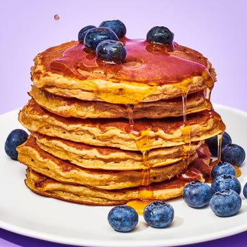 stacked pancakes on a plate with blueberries and syrup pouring on them, on a background