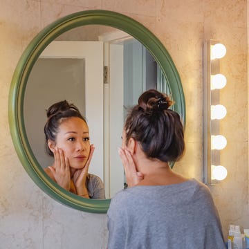 worried east asian woman checking her face skin in the mirror