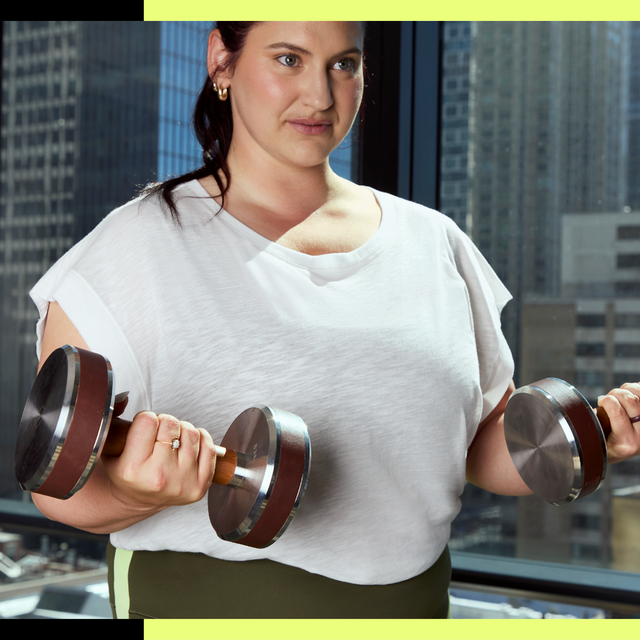 Person holding dumbbells in a city apartment with large windows.