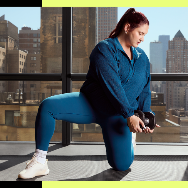 Person kneeling with dumbbell in a gym with city view.