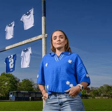 person in blue shirt stands near soccer field with jerseys hanging on goalposts.