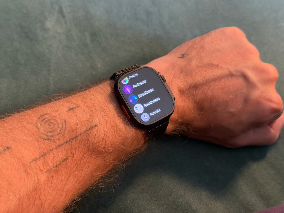 Smartwatch displaying apps on a wrist with tattoos visible on the forearm.