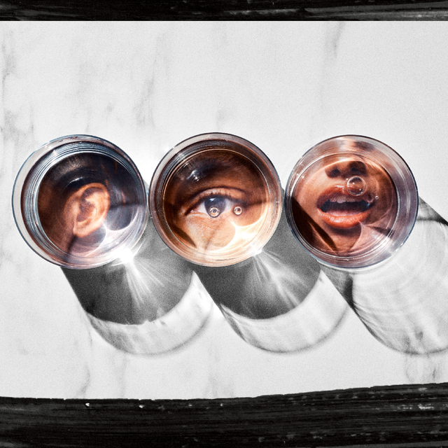 Three clear glasses reflect ears, an eye, and a mouth against a marbled background, casting shadows.