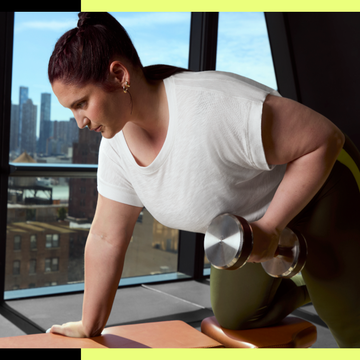 Woman doing a dumbbell row in a gym with city view.