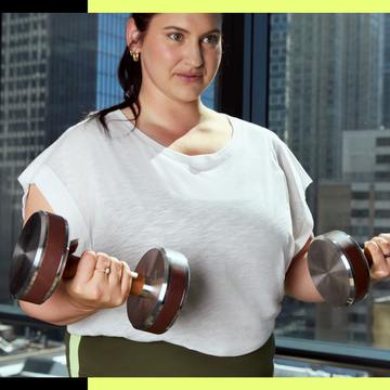 Person lifting dumbbells in gym with city view.
